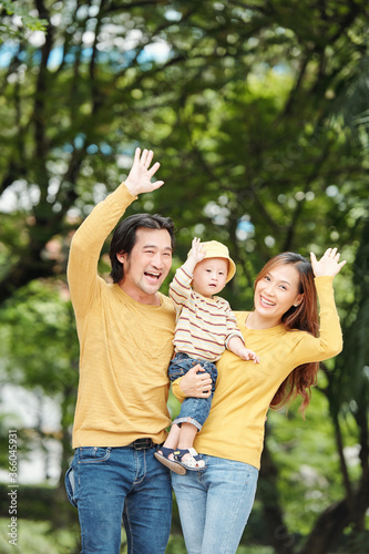 Happy smiling young Vietnamese man, woman and their child standing in park and waving with hand