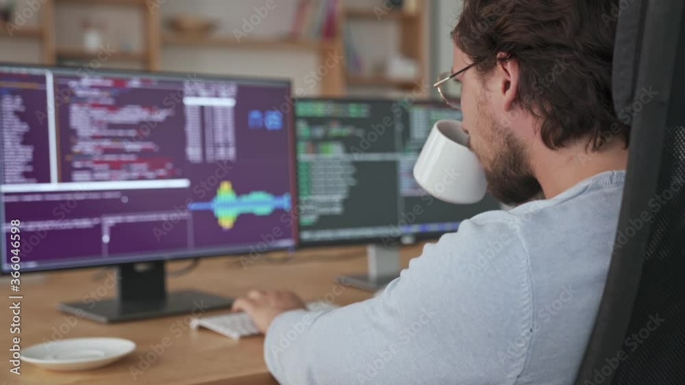 A back view of a young programmer is working with his computer sitting in the office