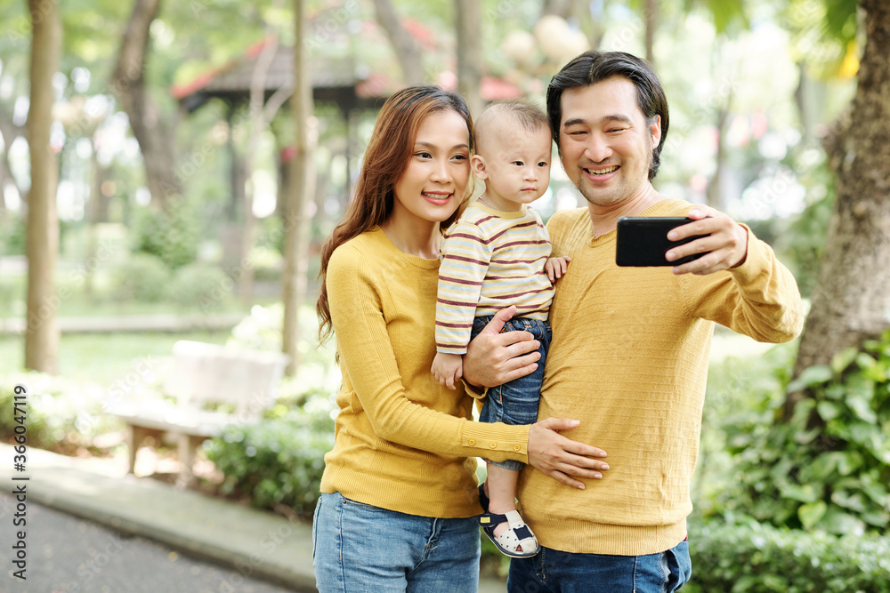 Happy young Asian family of three photographing together in park