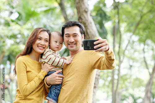 Happy positive Asian man taking selfie with his pretty wife and adorable little son © DragonImages
