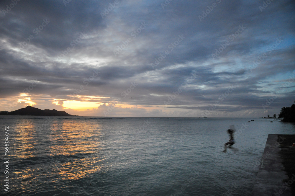 Children jumping in the water with dramatic overcast sky in a tropical sunset