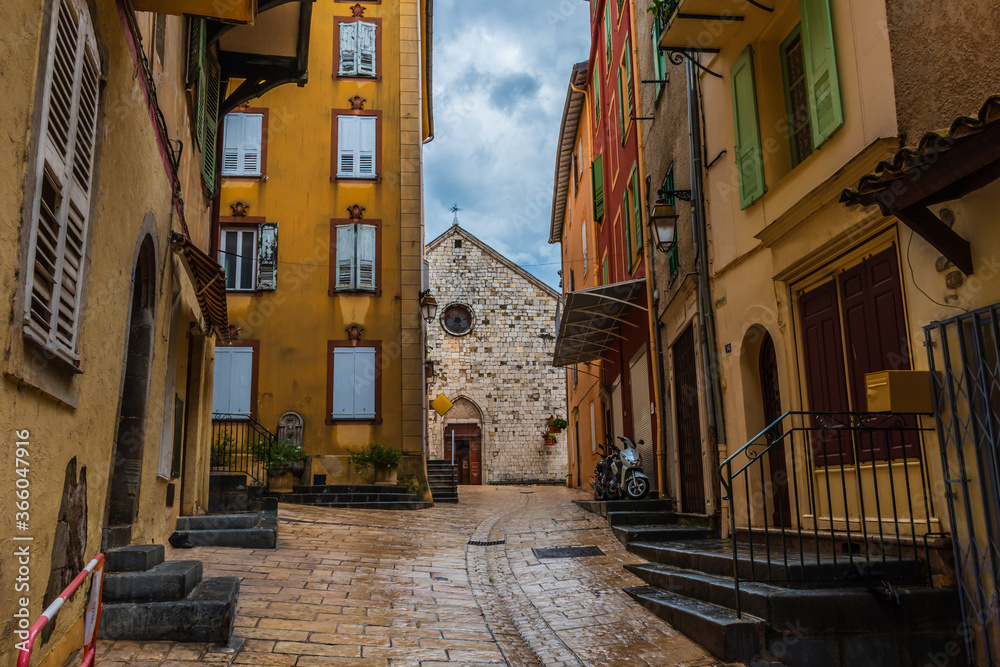 Obraz premium A picturesque wide angle view of a narrow street in a medieval French village in the Alps on a rainy day (Puget-Theniers, Alpes-Maritimes, Provence, France)