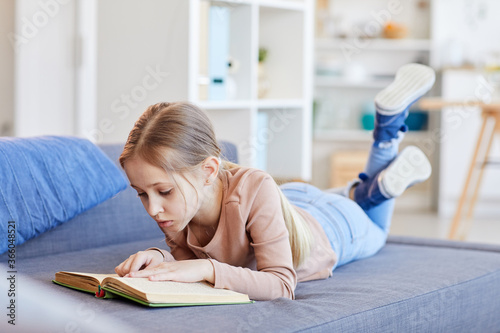 Cuadro en lienzo Full length portrait of cute blonde girl reading book or studying while lying on