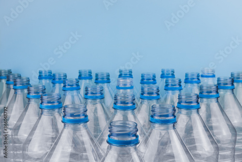 Empty clear plastic bottles without caps stacked on a blue background. Recycling and environment concept.