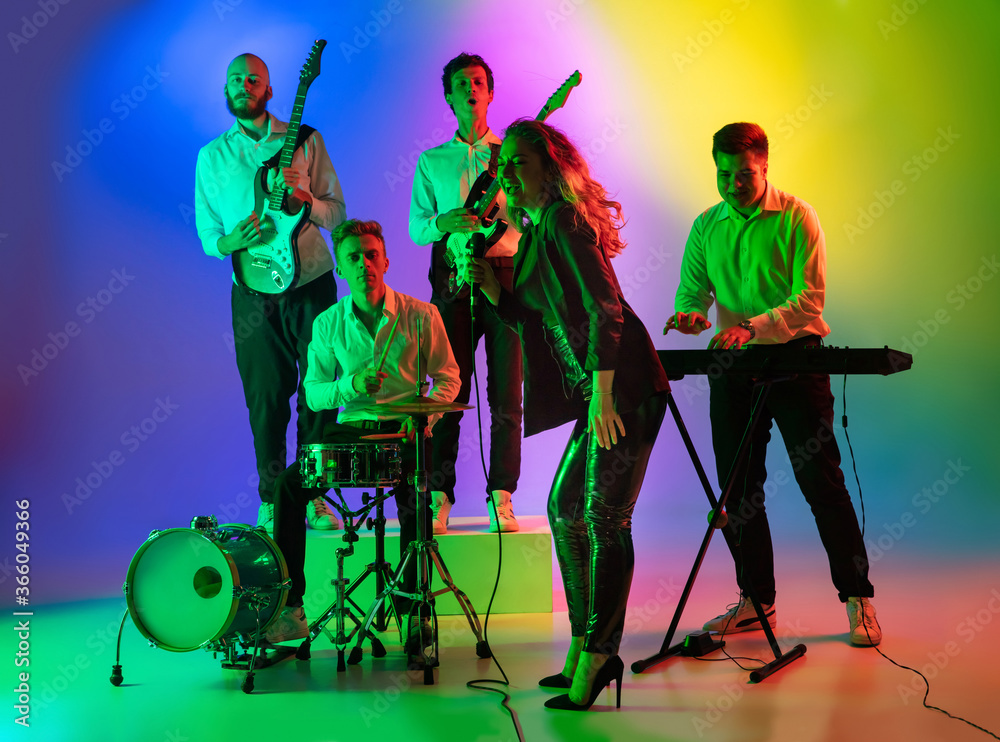 Fototapeta premium Motion. Young caucasian inspired and expressive musicians, band performing on multicolored background in neon. Concept of music, hobby, festival, art. Joyful artist, colorful, bright portrait.