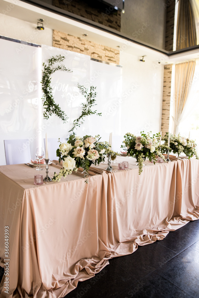 Side view of the presidium of the newlyweds at the wedding. Table for the bride and groom with flowers and candle in restaurant. Banquet table for newlyweds. Luxury wedding banquet decor