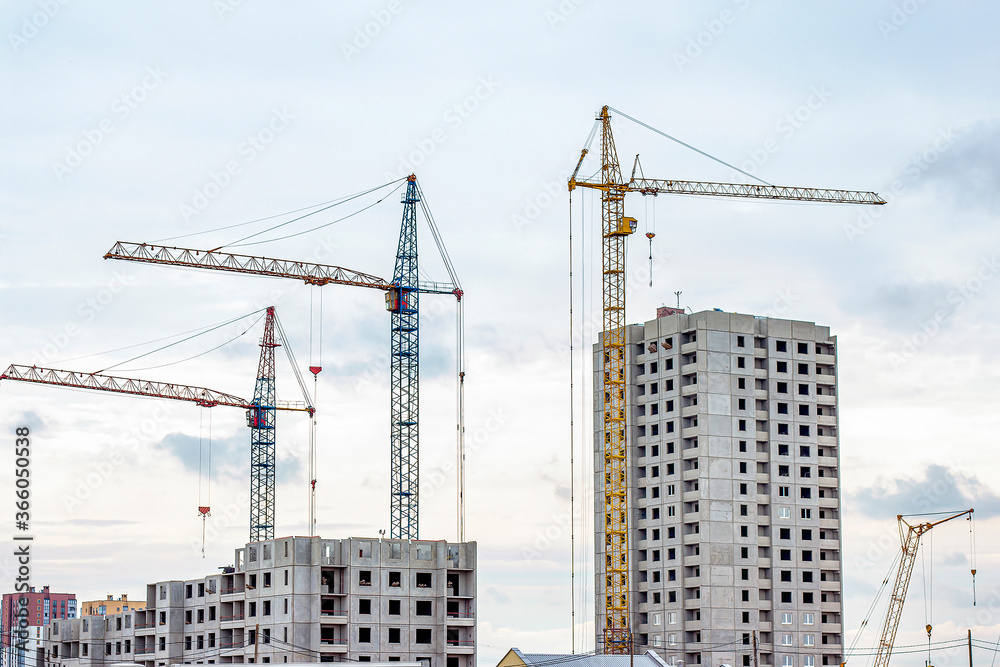 Construction site with the high cranes building a grey block house in the city. Construction site with the high cranes building a grey block house in the city.
