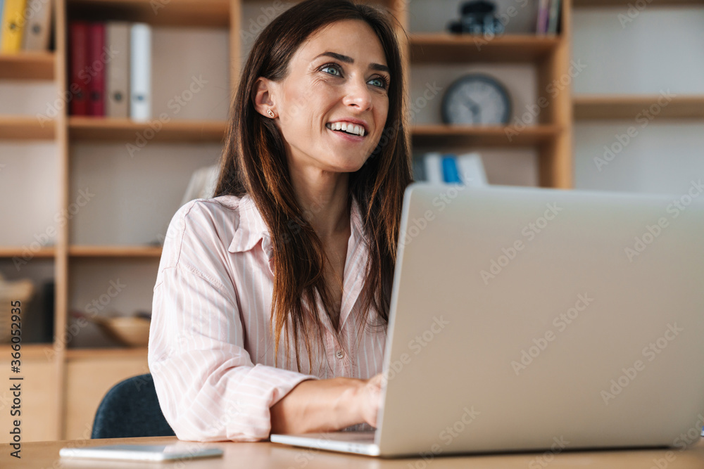 Image of happy businesswoman smiling while working with laptop Image of happy businesswoman smiling while working with laptop