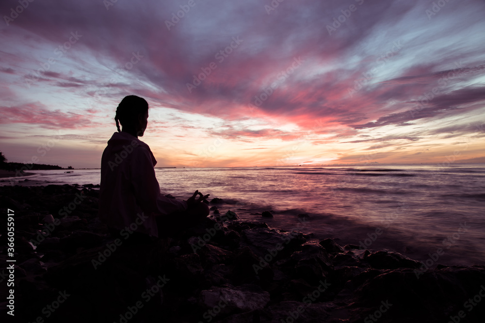 Silhouette of young woman wearing exercise clothes practicing yoga on the beach at sunset or sunrise. women do yoga. women exercising yoga in the beach.Young girl meditating in lotus posture. Silhouette of young woman wearing exercise clothes practicing yoga on the beach at sunset or sunrise. women do yoga. women exercising yoga in the beach.Young girl meditating in lotus posture.