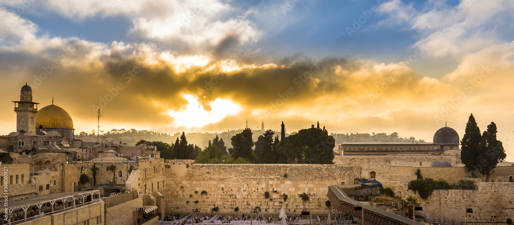 Fototapeta premium Beautiful sunrise clouds over the Mount of Olives and the Temple Mount sites: Dome of the Rock, Western Wall and Al Aqsa Mosque; with Jewish people praying in sections because of covid-19 regulations 
