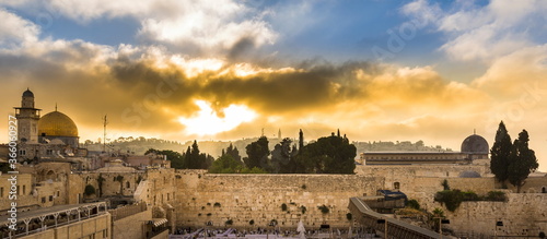 Beautiful sunrise clouds over the Mount of Olives and the Temple Mount sites: Dome of the Rock, Western Wall and Al Aqsa Mosque; with Jewish people praying in sections because of covid-19 regulations  photo