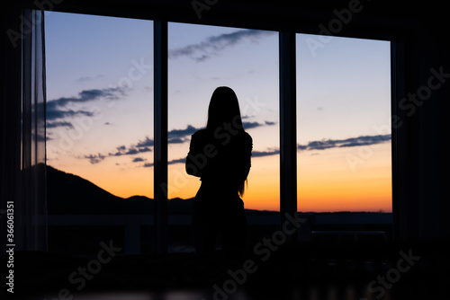Silhouette of a woman standing in front of a window with sunset in the background