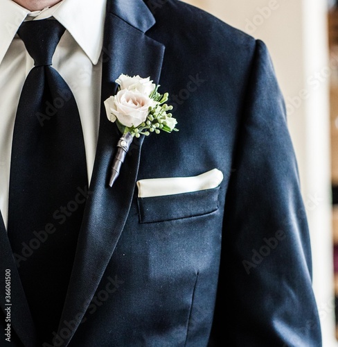 simple white rose boutonniere on lapel of groom's suit or tuxedo with black tie