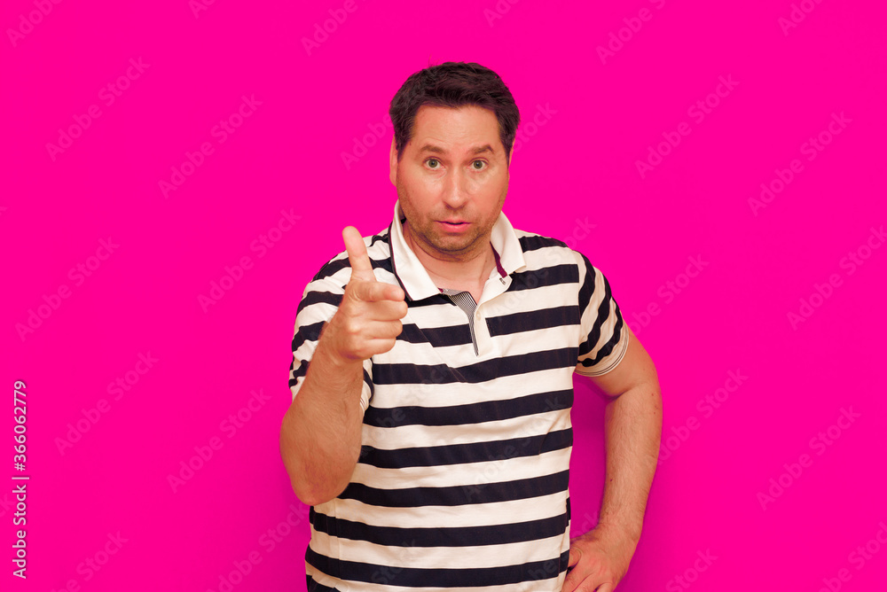 Joyful man in striped t-shirt gesturing index finger hand on camera isolated over magenta background Joyful man in striped t-shirt gesturing index finger hand on camera isolated over magenta background
