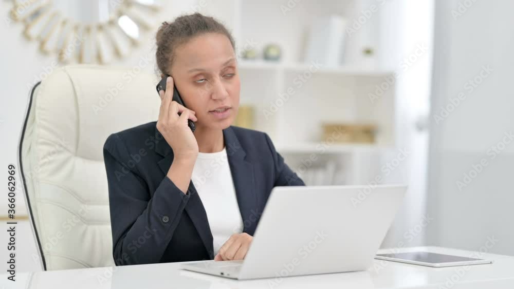 African Businesswoman with Laptop Talking on Smartphone in Office 