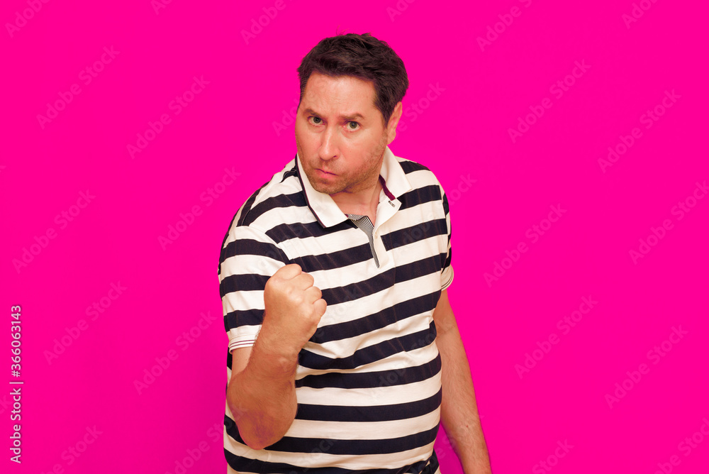 Joyful man in striped t-shirt gesturing index finger hand on camera isolated over magenta background Joyful man in striped t-shirt gesturing index finger hand on camera isolated over magenta background