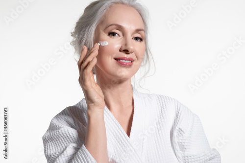 Smiling elderly woman with grey hair applying anti-aging cream.  photo