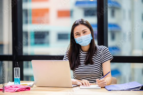 Asian women wear masks protect against airborne disease and salivary infections, during outbreak of Covid 19 virus (Coronavirus) and working with laptop in office, alcohol wash hands put on table.