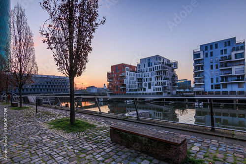 Morning mood on the West Harbor Canal in Frankfurt am Main. Residential area before sunrise with blue sky. Boats in the harbor and footpath with trees and reflection in the water