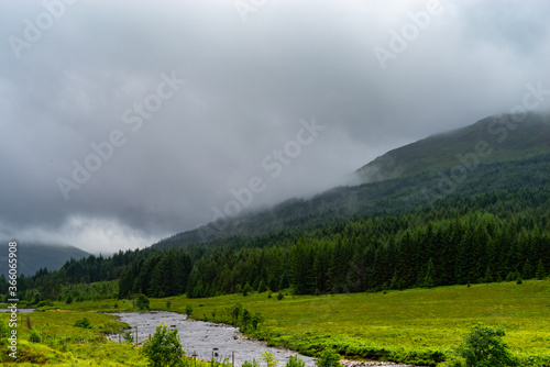Hills covered with trees with clouds blanket and a stream in the first plan.