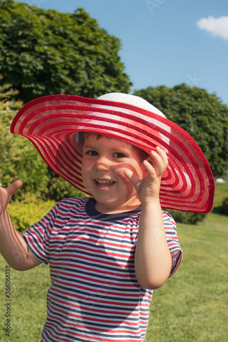 A 3-year-old boy in a red hat and a striped T-shirt. Happy childhood in the summer. Sun protection for children