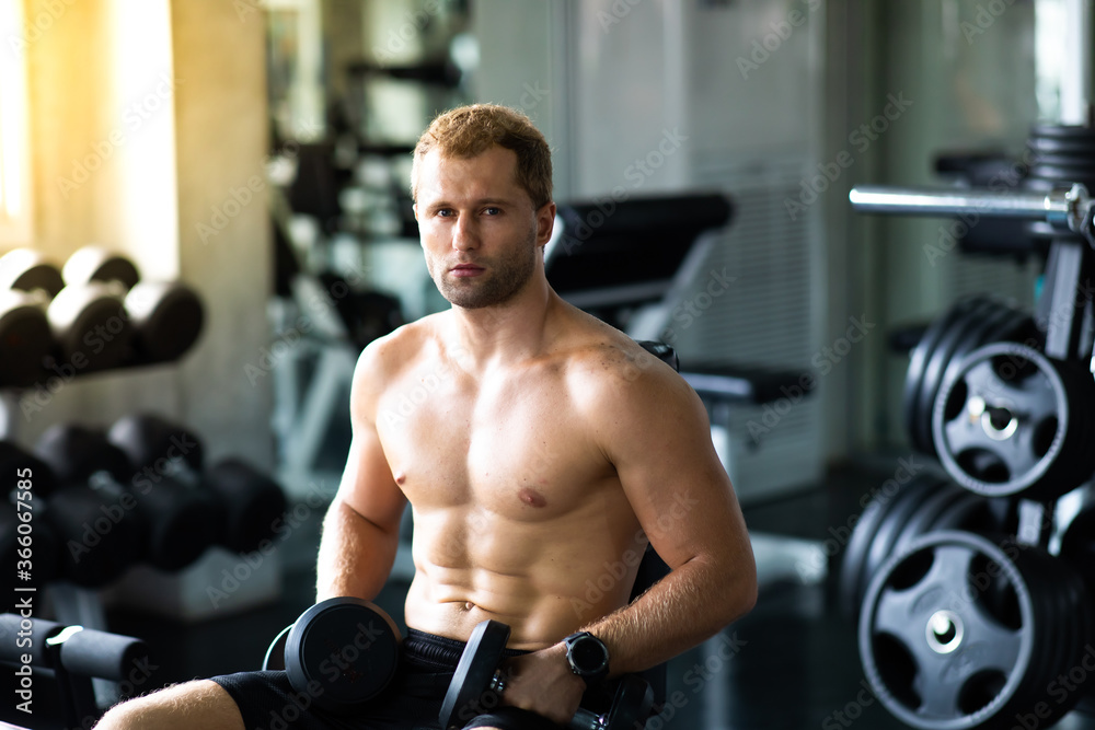 Naklejka premium Young Man Naked bodybuilder exercising lifting with dumbbell at gym. .Gym equipment and sport concept. Fitness Healthy lifestye and workout at gym concept.