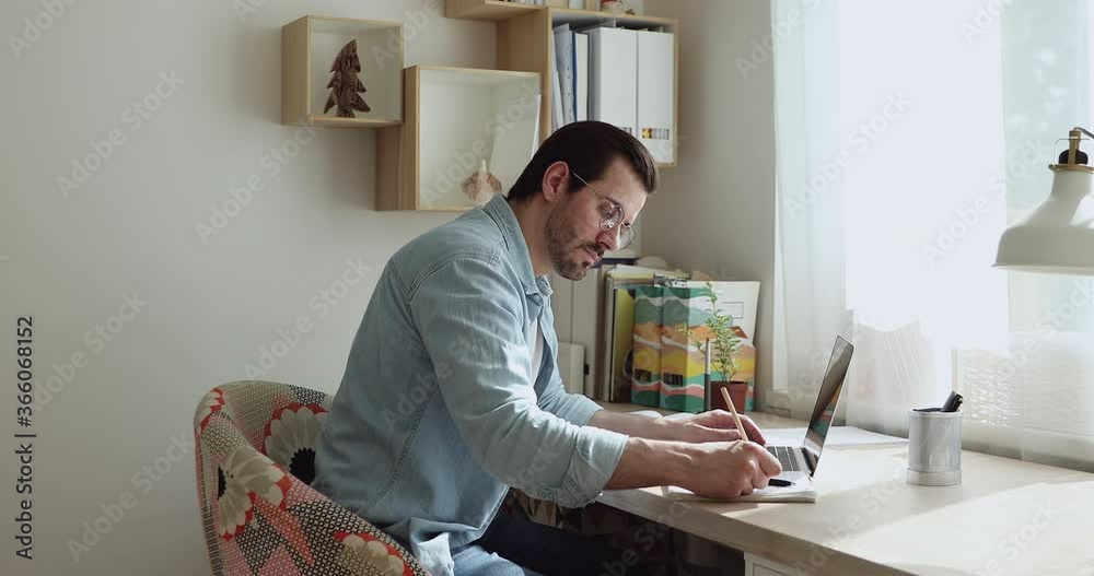 Man sit at desk working on research, new project, typing on laptop, take useful important information from network, makes notes writes down on notebook. Self-education process, internet usage concept