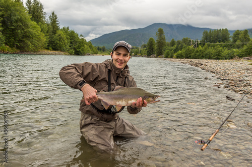 A fisherman holding up a male humpback pink salmon while wading in a river.
