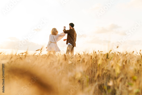 Image of young caucasian couple walking in golden field on countryside