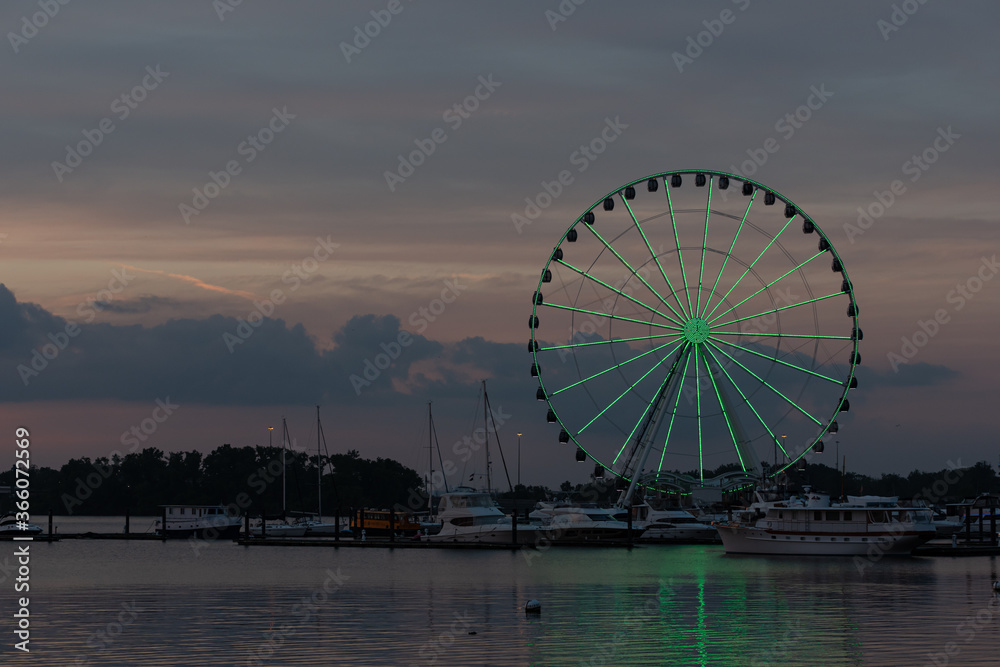 Brightly-lit Ferris wheel at twilight in a harbor