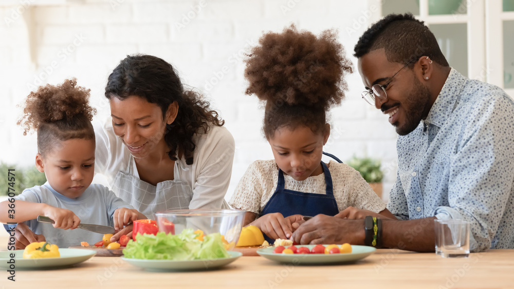 Loving young african American parents chop vegetables teach small ethnic children cooking at home, caring biracial mom and dad have fun preparing healthy food salad with little kids in kitchen Loving young african American parents chop vegetables teach small ethnic children cooking at home, caring biracial mom and dad have fun preparing healthy food salad with little kids in kitchen