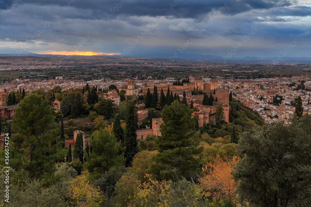 View over the city of Granada. Spanish city in Andalusia with dramatic sky at sunset. Historic Alhambra fortress with trees and buildings in the background