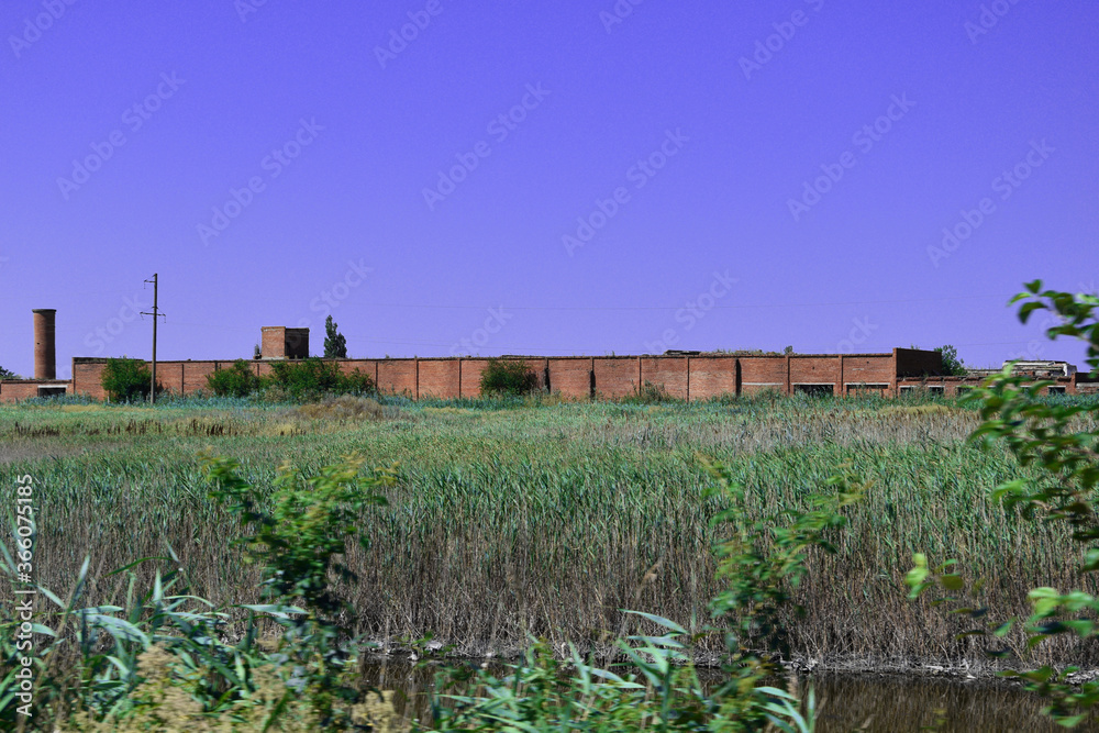 An old abandoned red brick factory stands on the bank of the river.