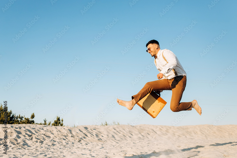 Crazy guy in a white shirt with suspenders jumps with a suitcase on the background of the lake, sunset