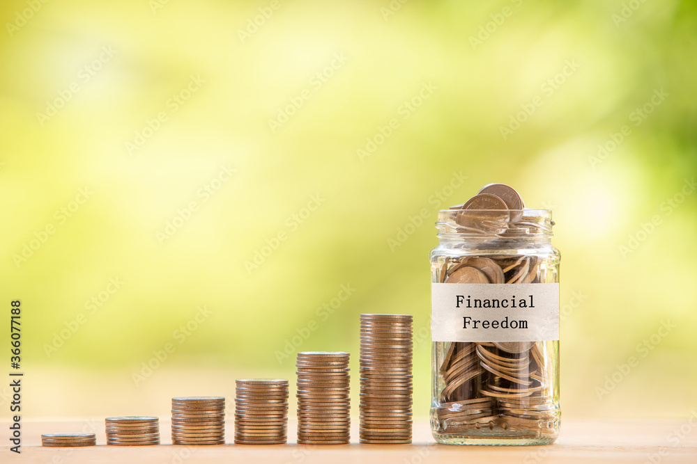 A glass jar filled with coins placed beside a pile of coins. Saving money for financial independence or financial freedom concept. - obrazy, fototapety, plakaty 