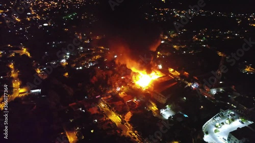 Aerial orbit, drone shot around a burning house. dark smoke and red fire blazing, due to riots and protests, during night time, in Los Angeles, California, USA photo