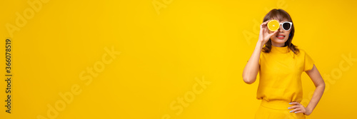 Portrait of woman holding orange and wearing white glasses isolated on yellow studio background