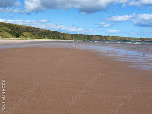 sandy beach on low tide, green hills visible at the distance
