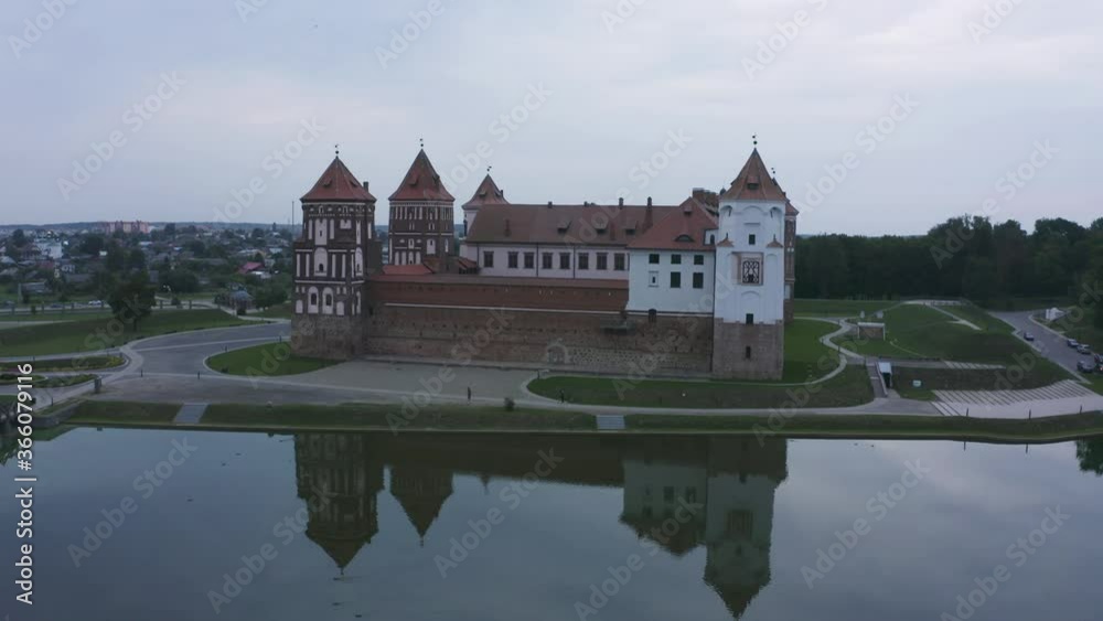 Mirsky Castle and its reflection in the lake in summer. Sunset in cloudy weather with rain clouds. Aerial view from a drone. Mirsky Castle and its reflection in the lake in summer. Sunset in cloudy weather with rain clouds. Aerial view from a drone.