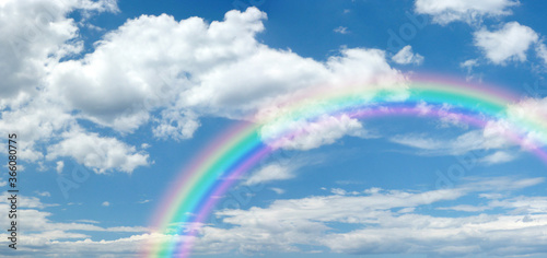 Sunny summer blue sky panoramic rainbow - big fluffy clouds with a giant arcing rainbow against a beautiful summertime blue sky with copy space for messages 