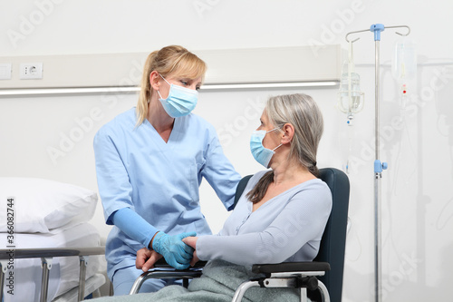 nurse take comfort elderly woman in wheelchair wearing surgical protective medical masks in hospital room  concept of isolation from corona virus covid 19