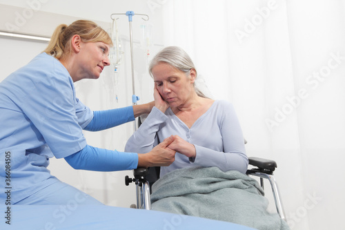 smiling nurse take comfort elderly woman isolated on wheelchair near bed in hospital room, concept of loneliness and old age diseases