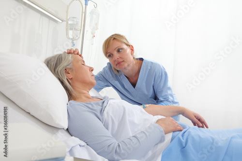 nurse take comfort elderly woman lying in the hospital room bed, by stroking her and holding the arm where the drip needle is, concept of loneliness and old age diseases