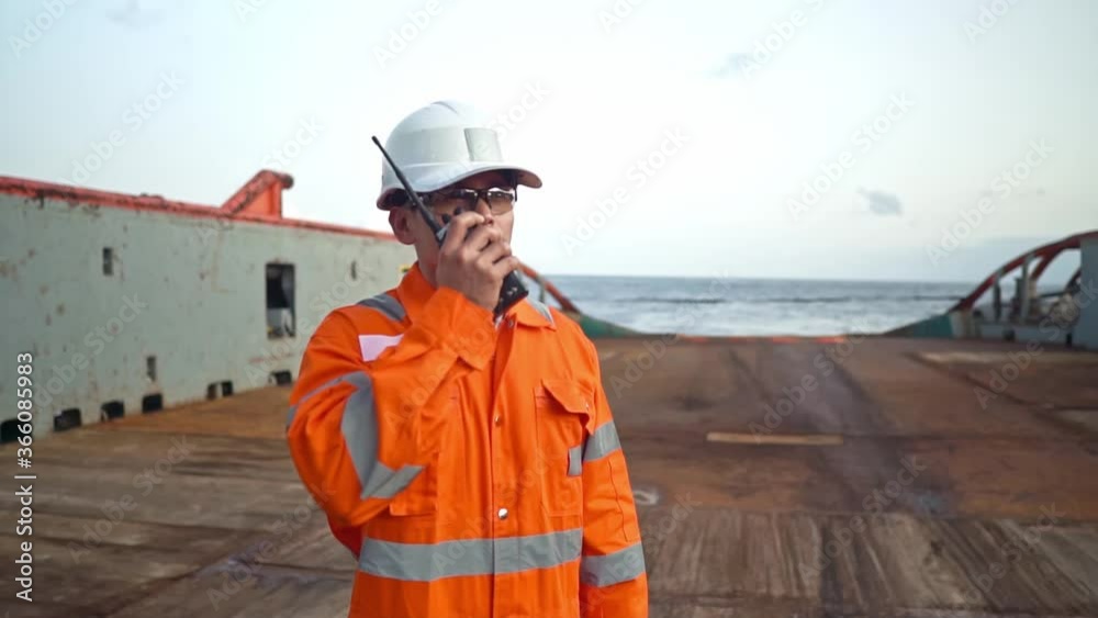 Filipino deck Officer on deck of vessel or ship , wearing PPE personal protective equipment. He speaks to VHF walkie-talkie radio in hands. Dream work at sea Filipino deck Officer on deck of vessel or ship , wearing PPE personal protective equipment. He speaks to VHF walkie-talkie radio in hands. Dream work at sea