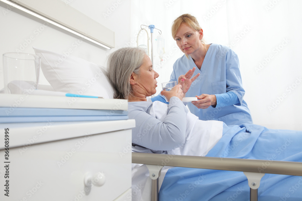 Obraz premium nurse gives the pill to the elderly woman patient lying in the hospital room bed, concept of loneliness and old age diseases