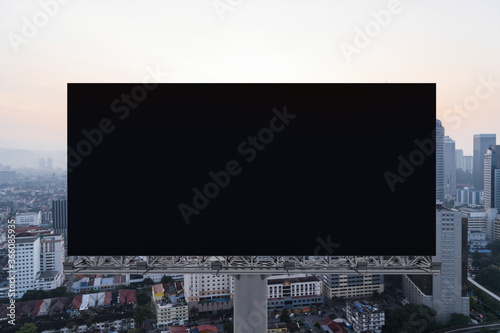 Blank black road billboard with Kuala Lumpur cityscape background at sunset. Street advertising poster, mock up, 3D rendering. Front view.