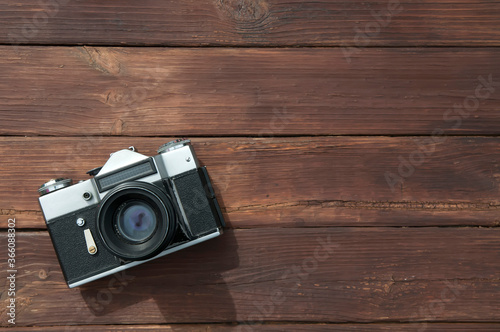 an old retro film camera with scratches dust and a black lens on a wooden table made of planks with copy space in the lower left corner of the image