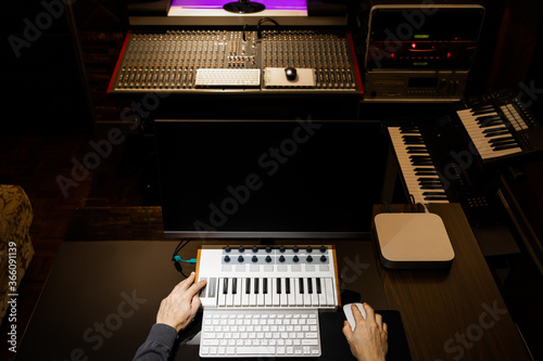 top view of male music producer hands working on midi keyboard and computer in recording studio