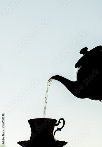 Tea being surved in a beautiful cup and saucer, silhouette against a blue background photo