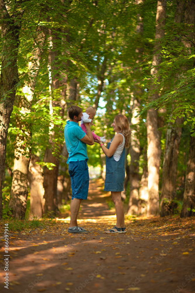 Mother, father and baby walking in the park. Summer time. Happy family spent time together outdoors. Man holds his daughter in the arms.